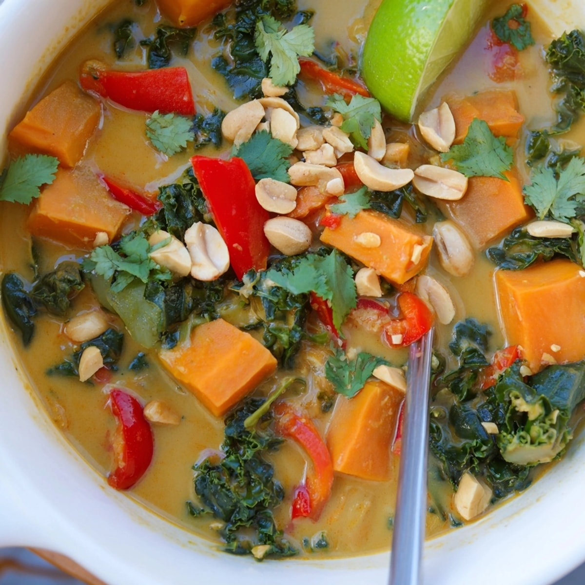 Bowl of vibrant Thai Peanut Kale Veggie Stew, garnished with cilantro and peanuts.