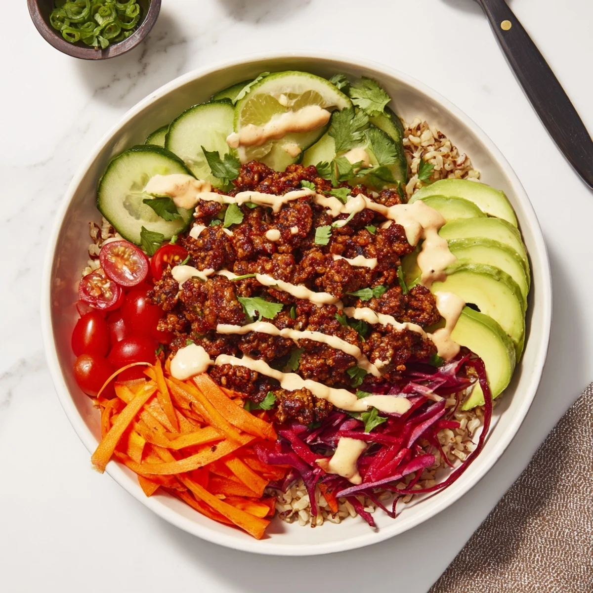 Vibrant plant-based meat bowl topped with avocado, carrots, and spicy mayo drizzle.  