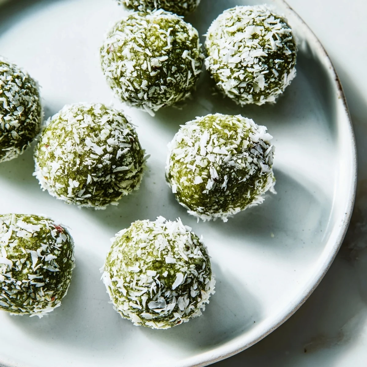 Creamy coconut matcha snowball fat bombs, rolled in shredded coconut, a low-carb keto dessert.