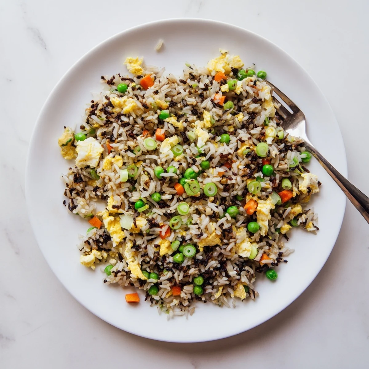 A close-up of black garlic fried rice reveals caramelized garlic bits, fluffy grains, and colorful mixed vegetables on a plate.