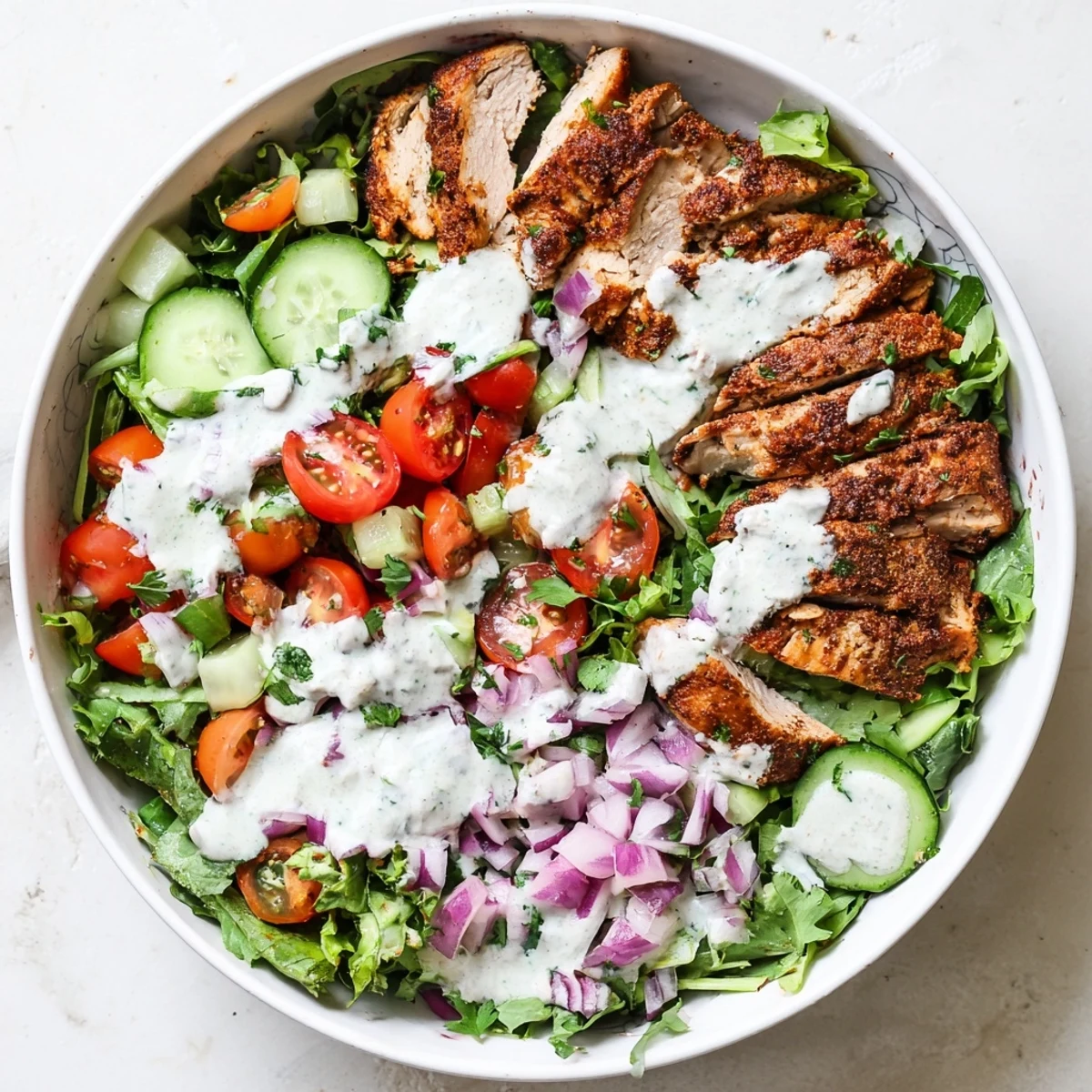 A vibrant Chicken Shawarma Salad Bowl with spiced, juicy chicken atop crisp greens, cucumbers, tomatoes, and a drizzle of tangy garlic sauce.