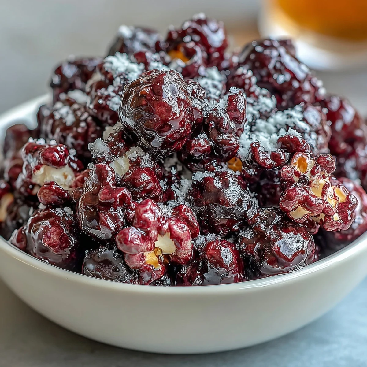 Glossy kettle corn coated in tangy black currant cheesecake powder, piled high in a white ceramic serving bowl for a sweet snack.