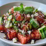 Freshly cubed watermelon and cucumber tossed with mint, feta, and a drizzle of balsamic glaze in a white bowl.