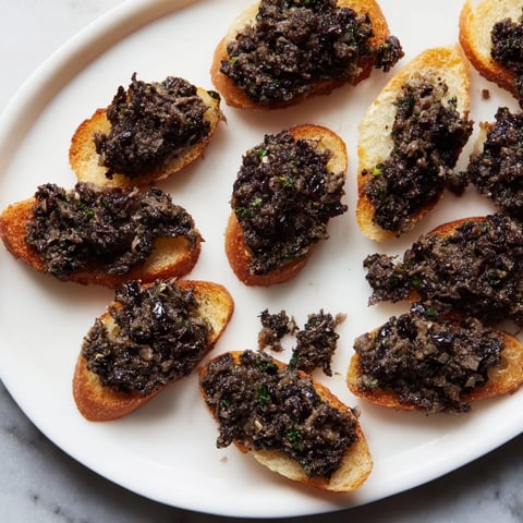 Golden crostini topped with vibrant black olive tapenade, a savory appetizer perfect for sharing.
