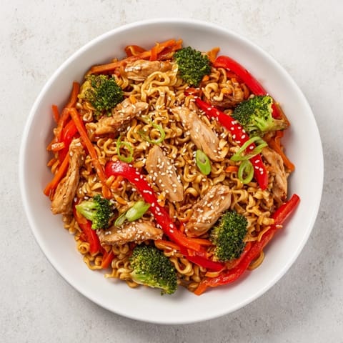 This image shows a sheet-pan crispy ramen, featuring golden chicken, vibrant vegetables, and crispy noodles.