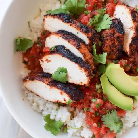 A deconstructed Spicy Chicken Burrito Bowl showing grilled chicken slices over rice, beans, corn, and zesty salsa.