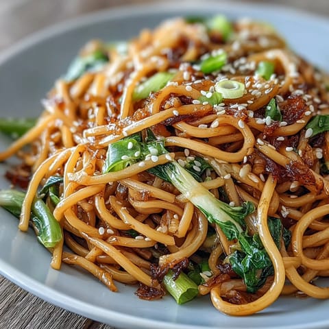 Aromatic ginger-scallion noodles tossed with silky wheat noodles and sautéed greens, garnished with sesame seeds and fresh chili slices.