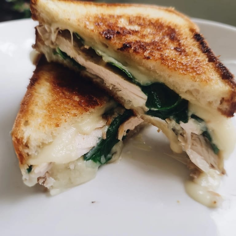 A perfectly pressed Grilled Chicken Spinach Panini cut in half, revealing layers of juicy chicken, wilted spinach, and gooey Parmesan.