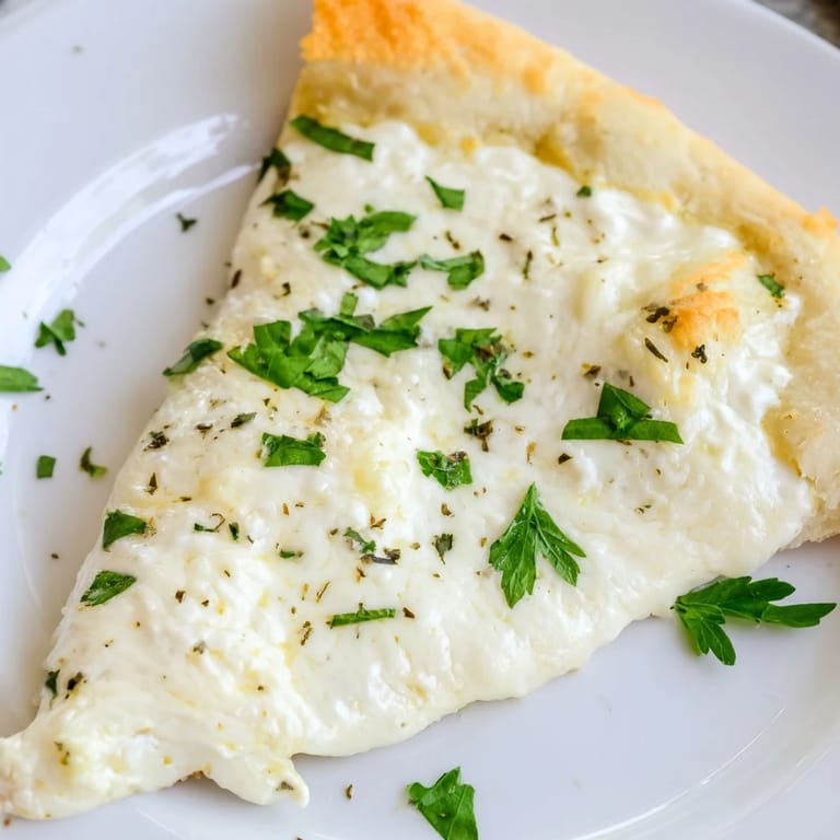 Slice of Creamy Garlic White Pizza on a marble surface, with velvety garlic cream sauce visible and parsley garnish.