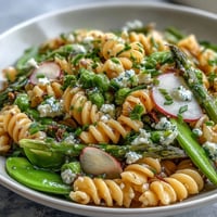 Spring pasta salad with lemon vinaigrette and radishes in a white serving bowl.